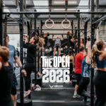 Gruppo di atleti in un box CrossFit italiano durante un workout dei CrossFit Open 2026 con pubblico che fa il tifo.