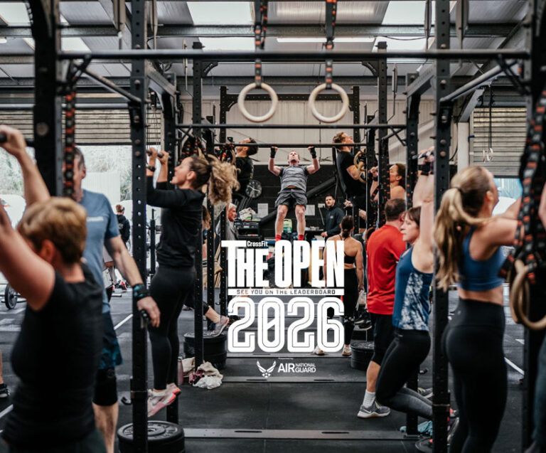 Gruppo di atleti in un box CrossFit italiano durante un workout dei CrossFit Open 2026 con pubblico che fa il tifo.